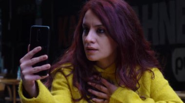 Dışarıda görüntülü konuşma yapan kızgın kızıl saçlı güzel kadının portresi. Çevrimiçi çatışma. Mesafe iletişimi sorunu. Videodaki kızıl saçlı kadına olan kıskançlık krizine kızgınım..