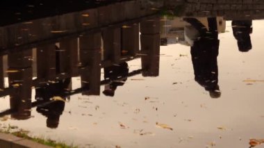 Köprüdeki yayaların su yansıması. Yağmurdan sonra sokak, alçak açı, su birikintisindeki yansımalara yakın çekim. 4K UHD arkaplan.