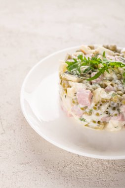 Beyaz tabakta tavuklu Olivier salatası.