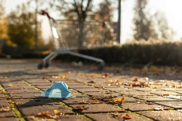 Grocery shopping with face mask during the coronavirus COVID-19 pandemic. Empty grocery shopping cart outdoor. Autumnal blurred background. Go shopping with a medical face mask.