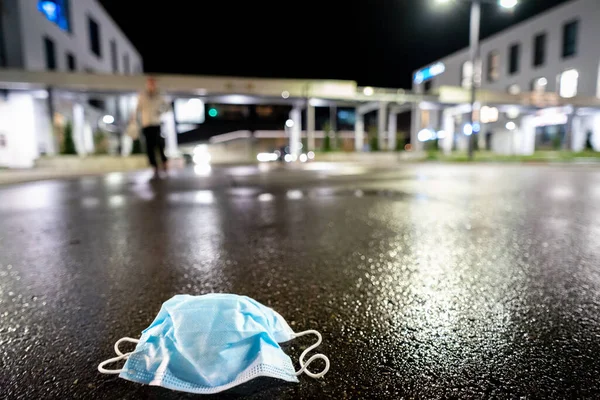 Fresh start concept in front of hospital. Protective mask on nature background with blurred clinic. Coronavirus protection. Medical protective mask on the ground. Covid-19. night shot.