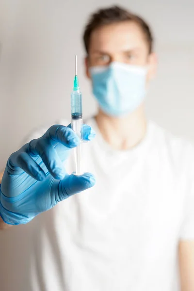 Doctor with medical face mask and medical gloves with a raised syringe, for vaccination close up