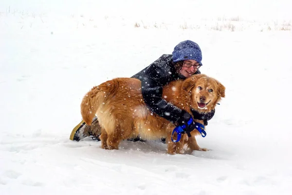 Junge Frau umarmt ihren glücklichen Hund im fallenden Schnee — Stockfoto