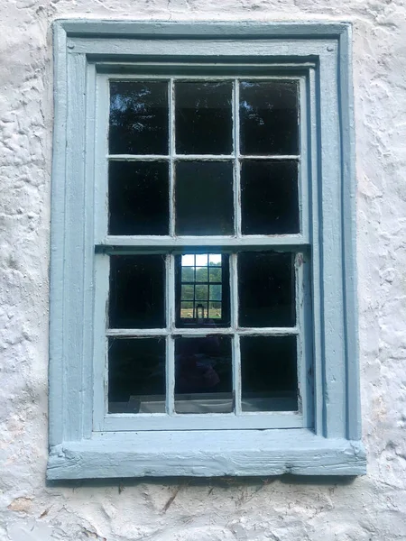Blå kolonialt 12-glasfönster i stenstuga med får utanför. — Stockfoto