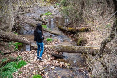 Genç adam devrilmiş ağaçlarla bahar deresinin kenarında duruyor..