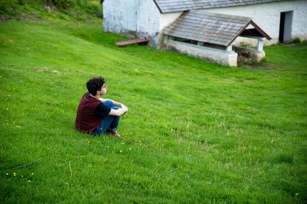 Young person sits alone in a grassy field looking into the distance — Stock Photo, Image