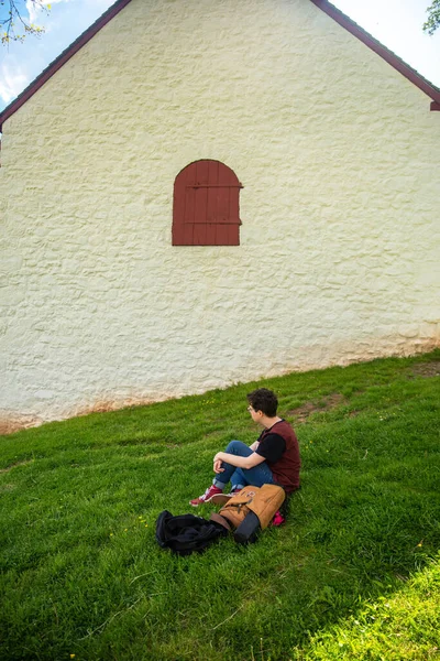 Una persona se sienta en la hierba por el granero colonial de piedra blanca con puerta roja — Foto de Stock