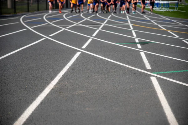 Biegacze ścigający się w kierunku kamery z linii startu na torze sportowym — Zdjęcie stockowe