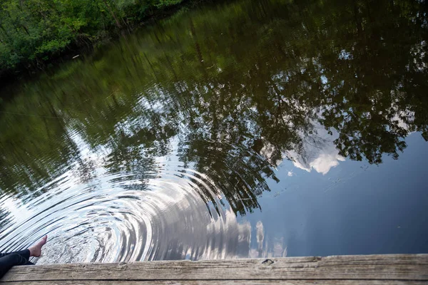 Füße baumeln im Waldteichwasser von einem hölzernen Steg und machen kreisförmige Wellen — Stockfoto