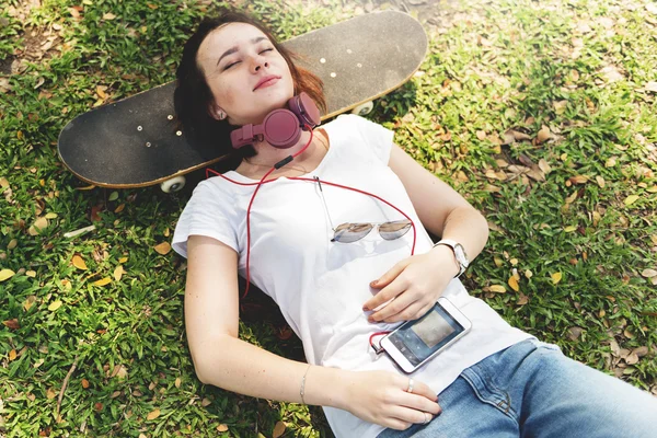 戴着耳机的女人躺在滑板上 — 图库照片