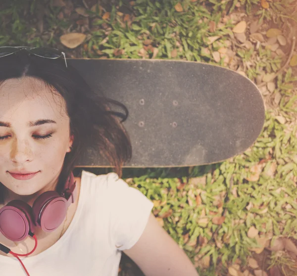 戴着耳机的女人躺在滑板上 — 图库照片