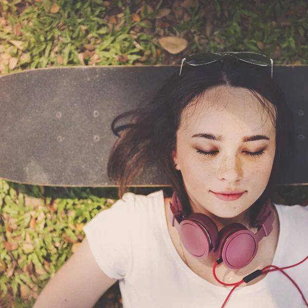 Vrouw met hoofdtelefoon ligt op skateboard — Stockfoto