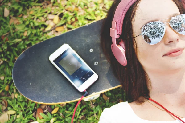 Жінка з навушниками лежить на скейтборді — стокове фото