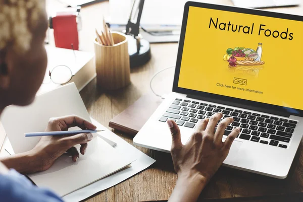 Vrouw die op laptop met natuurlijke voedingsmiddelen werkt — Stockfoto