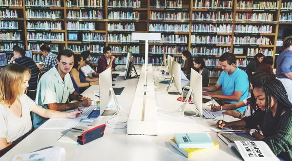 Студенты, использующие компьютеры в университетской библиотеке — стоковое фото