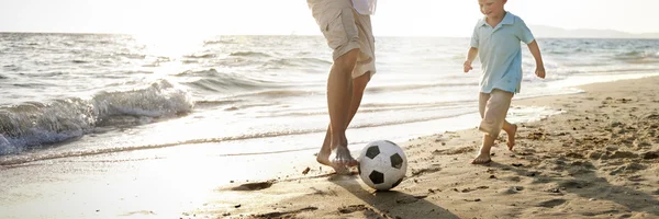 Far och son som spelar fotboll på stranden — Stockfoto