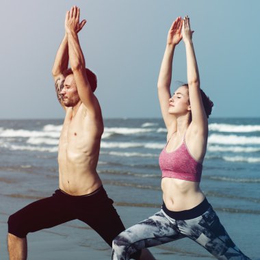 Çiftler plajda yoga yapıyor.