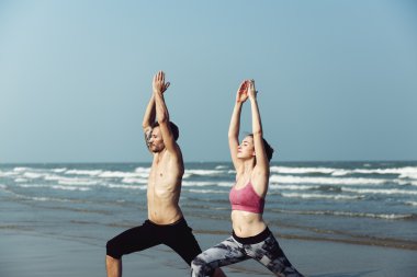 Çiftler plajda yoga yapıyor.