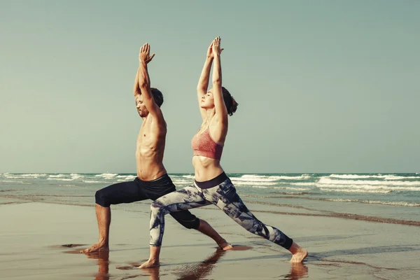 Par som gör yoga på stranden — Stockfoto