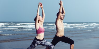 Çiftler plajda yoga yapıyor.