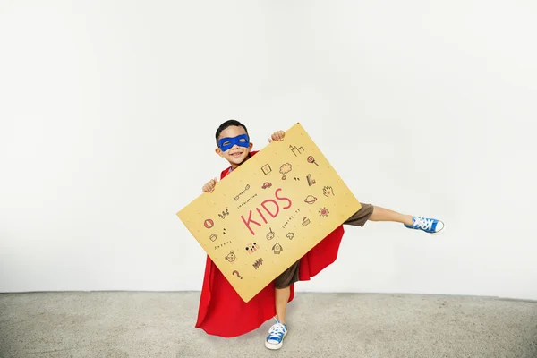 Мальчик-супергерой с картонкой в руках — стоковое фото