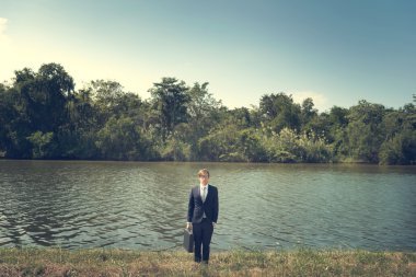 Evrak Çantası'nı ayakta nehrin yanında ile işadamı,