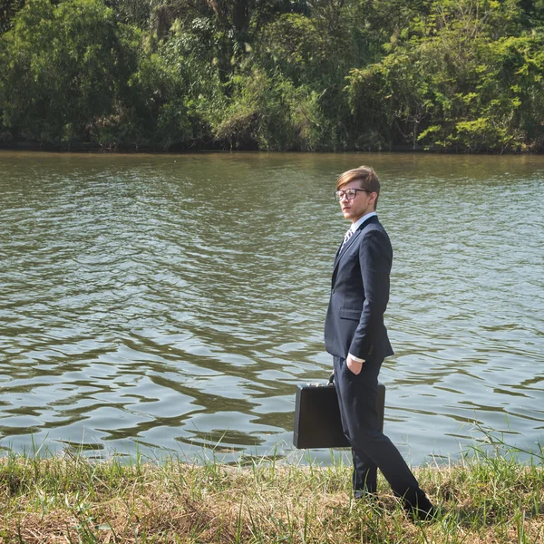 Businessman with briefcase at the river — Stock Photo, Image