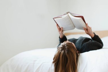 Woman reading a book on her bed during coronavirus quarantine clipart