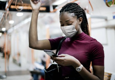 Otobüste maske takan Afro-Amerikalı bir kadın yeni normal bir şekilde toplu taşıma araçları kullanıyor.