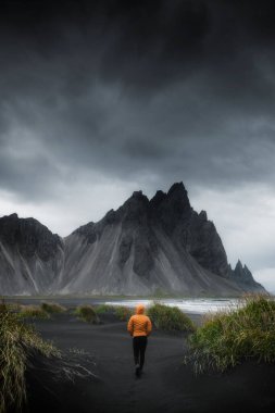 İzlanda 'da, kara kumsalda yürüyen bir adam.
