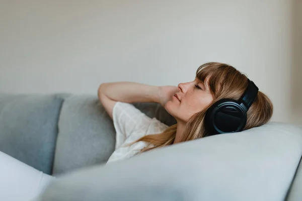 ソファの上でコロナウイルスの隔離中に音楽を聴く女性 — ストック写真