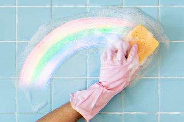 Pembe eldivenli bir kadın banyo fayanslarını fırçalıyor.
