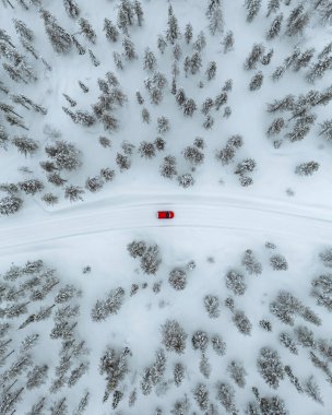 Drone view of a red car driving though a snowy forest in Lapland, Finland clipart