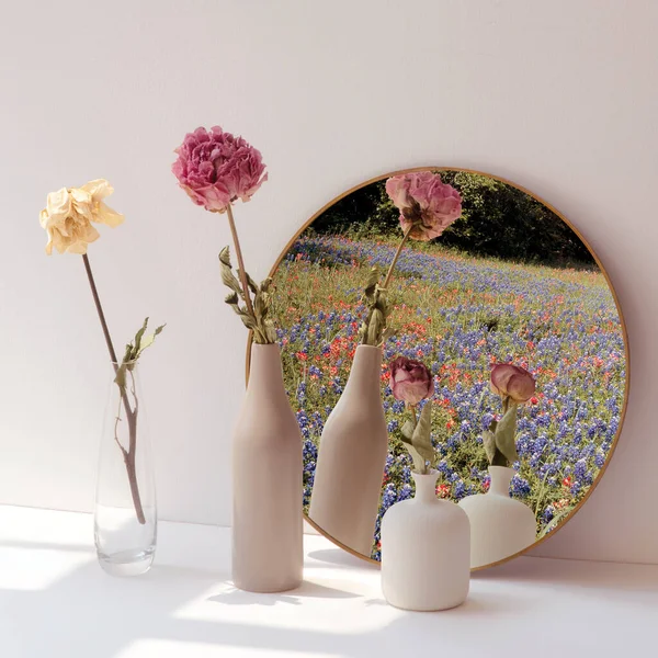 Dried flowers in minimal vases by a round mirror