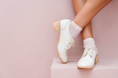 Bacak bacak üstüne atmış, beyaz Oxford ayakkabısı giyiyor.