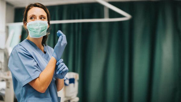 Женщина-медсестра в маске надевает перчатки и готовится вылечить пациента с коронавирусом