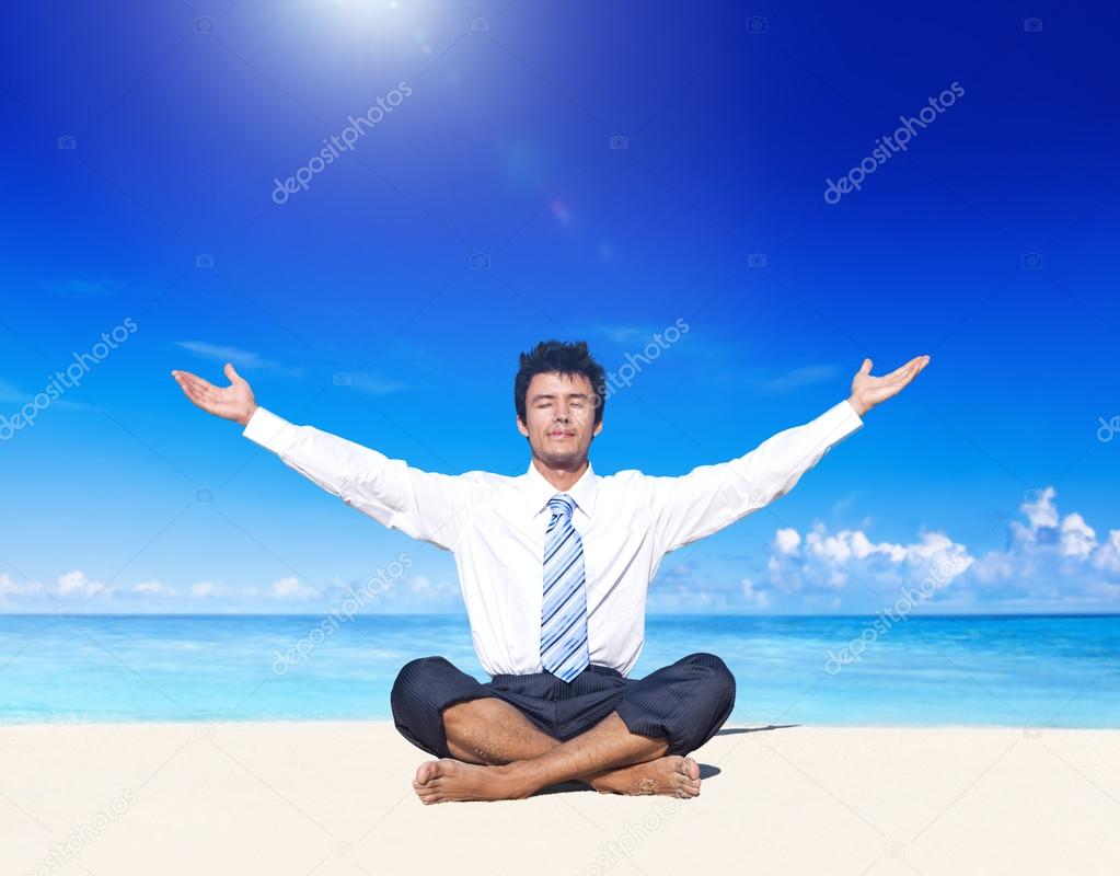 Businessman meditating on beach