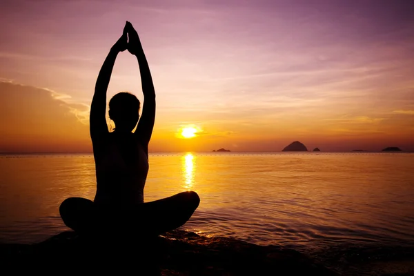 Woman meditating as sun sets over ocean — Stock Photo, Image