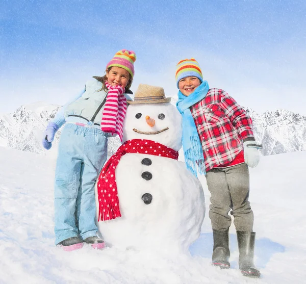 Sibilings posando ao lado de boneco de neve — Fotografia de Stock