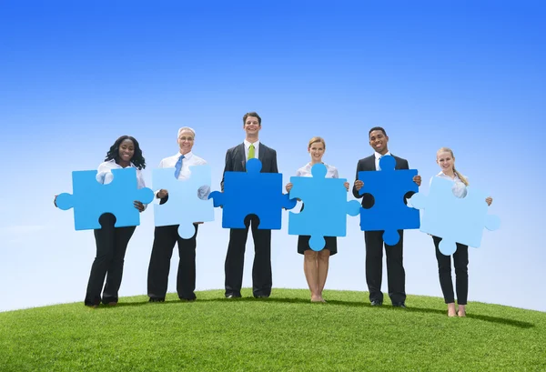 Business people holding puzzle on hill — Stock Photo, Image