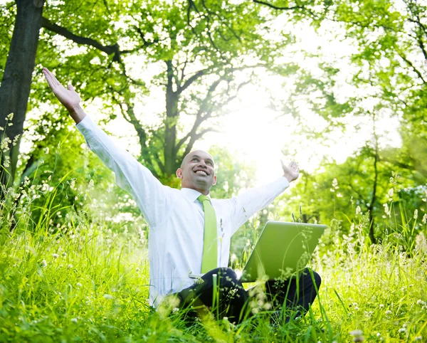 Бизнесмен сидит в лесу с ноутбуком Стоковое Фото