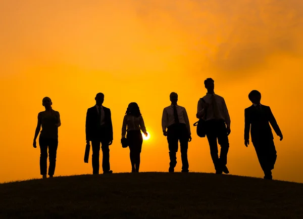 Business people walking on hill at sunset — Stock Photo, Image