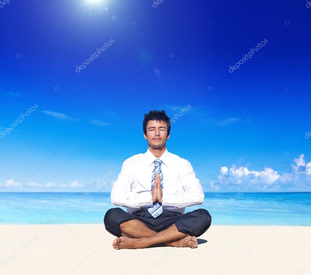 Businessman meditating on beach
