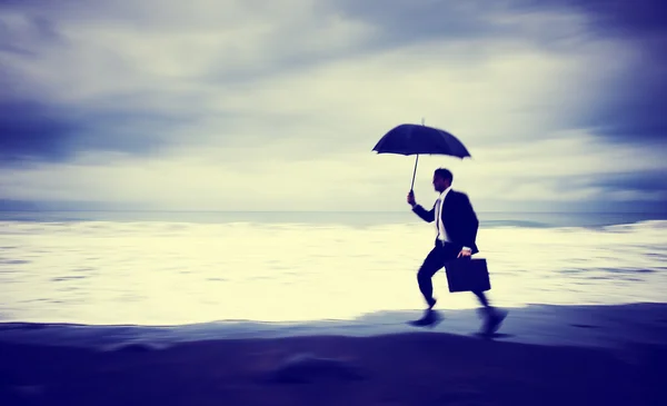 Besorgter Geschäftsmann läuft mit Sonnenschirm am Strand — Stockfoto