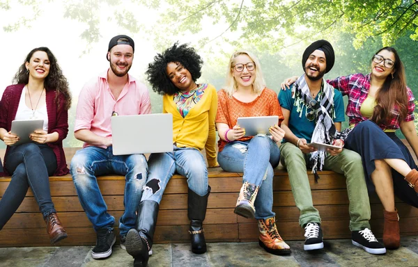 Amigos felices sentados en el banco con el ordenador portátil — Foto de Stock