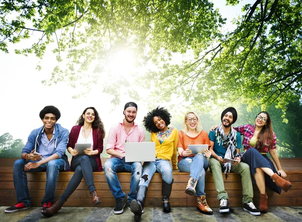 Happy friends sitting on bench with laptop — Stock Photo, Image