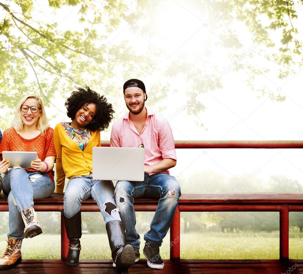 happy friends sitting on bench with laptop