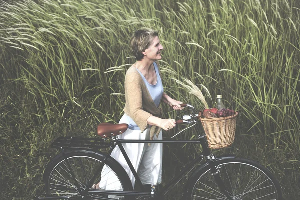 Starsza kobieta z rowerów w dziedzinie — Zdjęcie stockowe