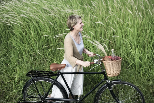 Starsza kobieta z rowerów w dziedzinie — Zdjęcie stockowe
