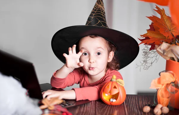 funny child girl in witch costume for Halloween using a digital tablet laptop notebook. Online call friends or parents